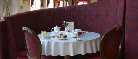 A dining area with a round table, red upholstered booth seating, and a white tablecloth.