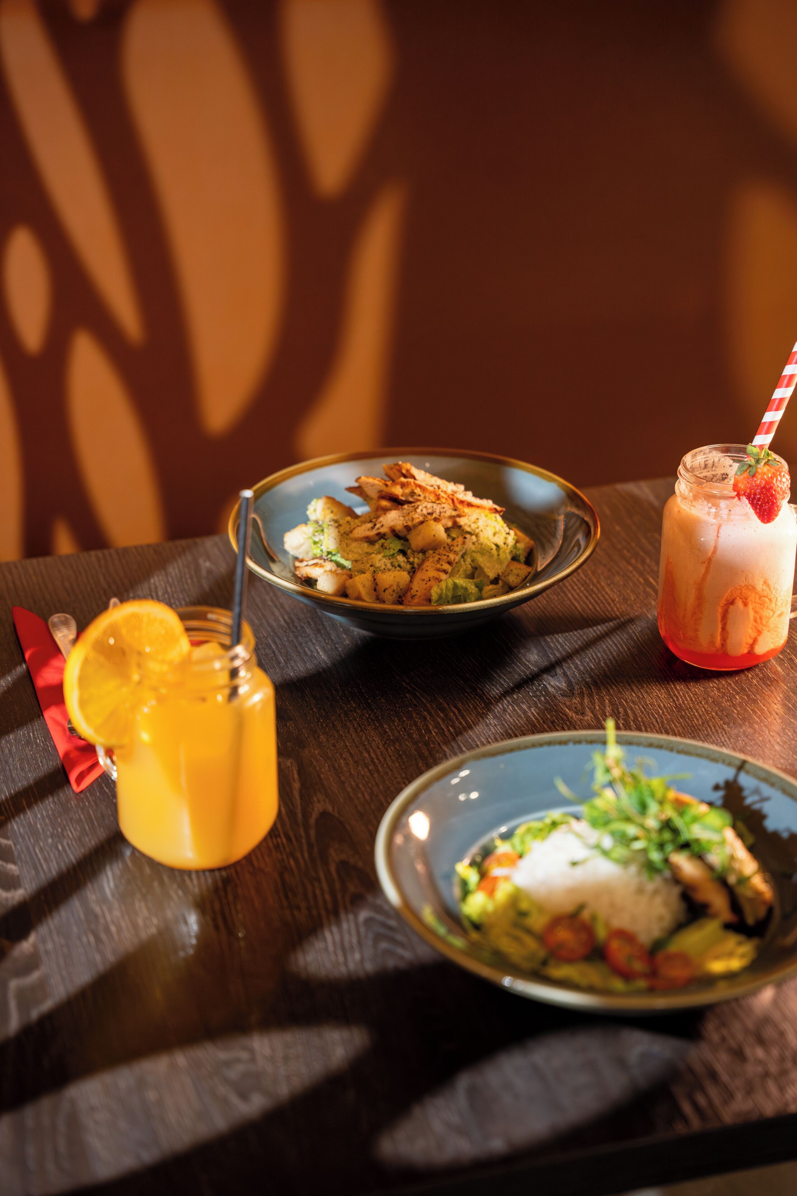 A table with a plate of food, a drink with a straw, and a glass of juice.