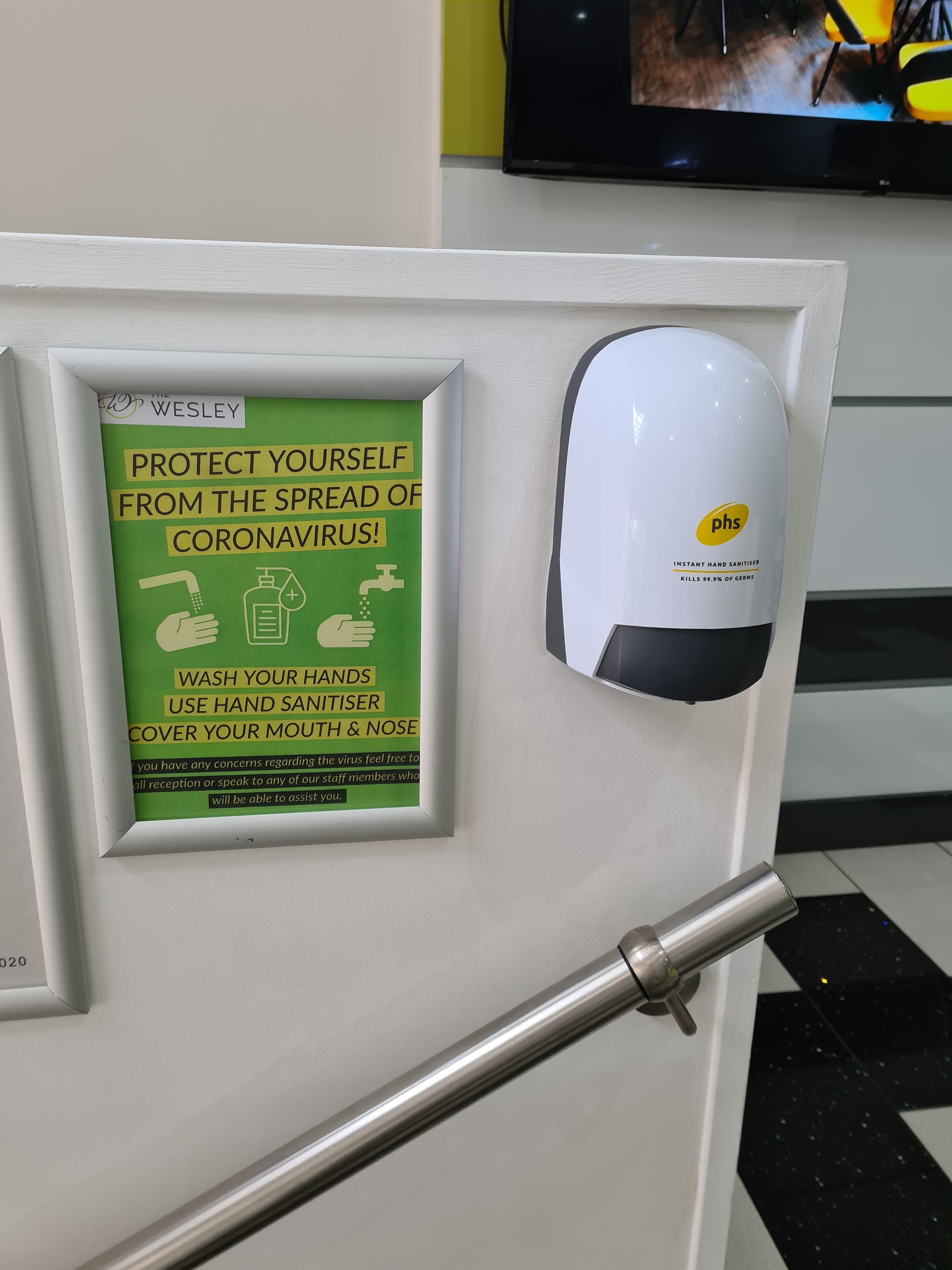 A hand sanitizer dispenser mounted on a wall with a sign advising on coronavirus protection.