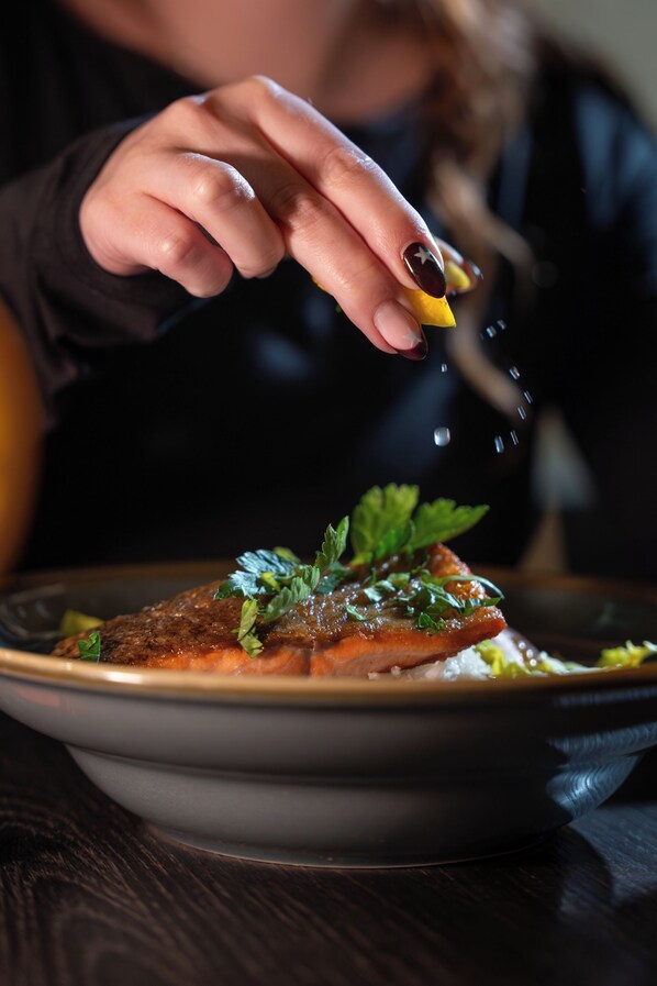 A person holding a lemon wedge over a plate of food.