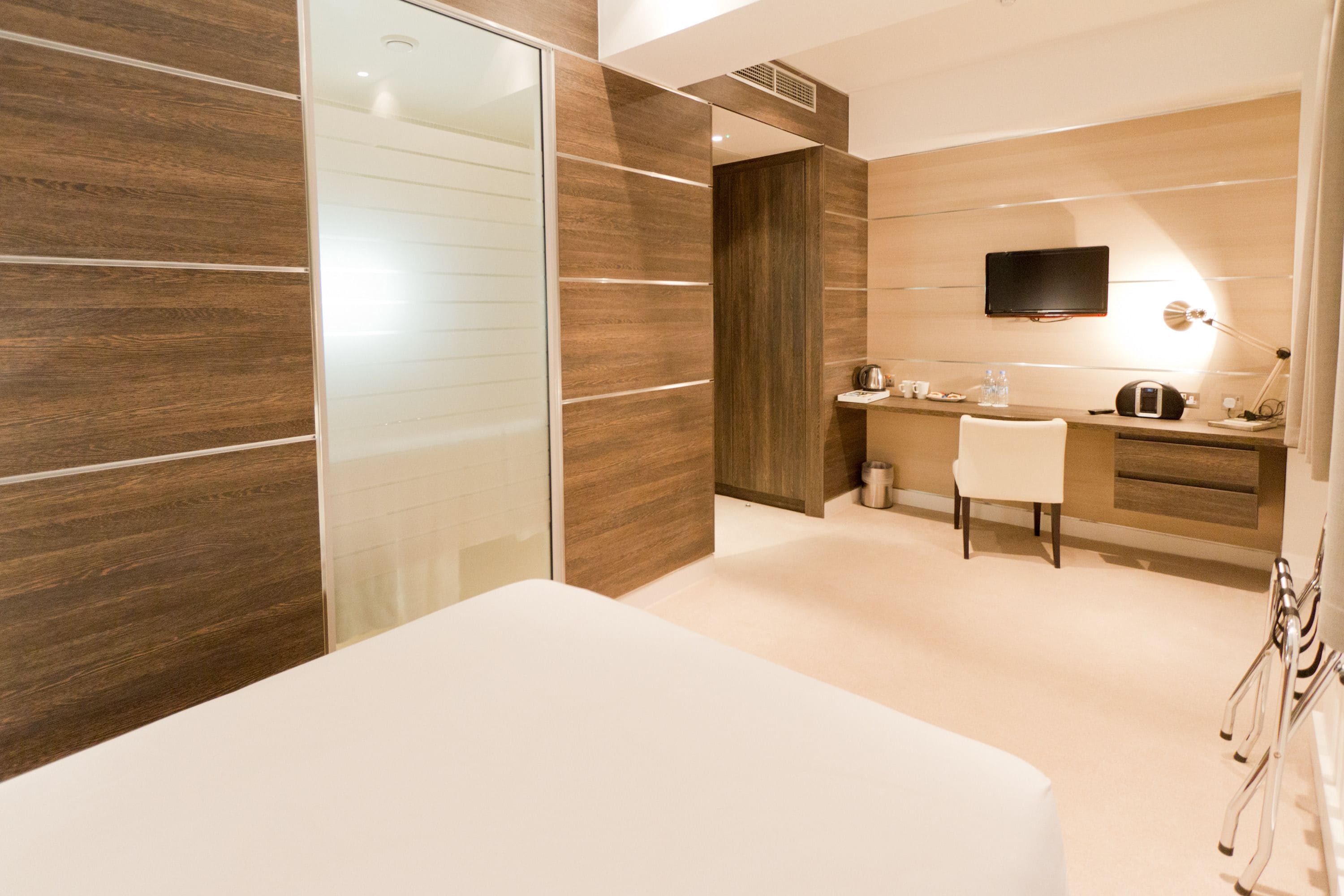 A modern bedroom with a large bed, a desk, and a TV mounted on the wall.