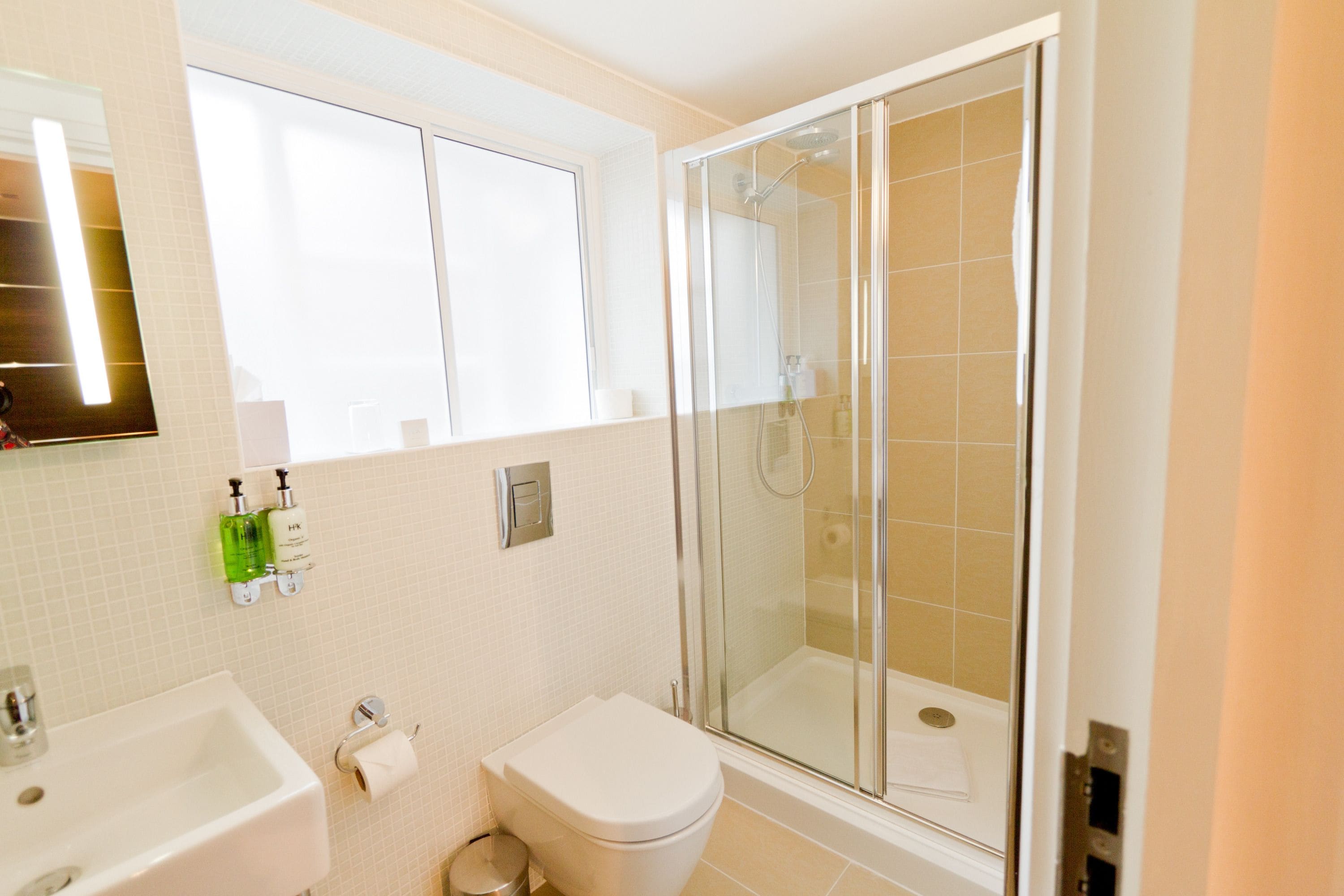 Un baño con inodoro, lavamanos y ducha con mampara de vidrio.
