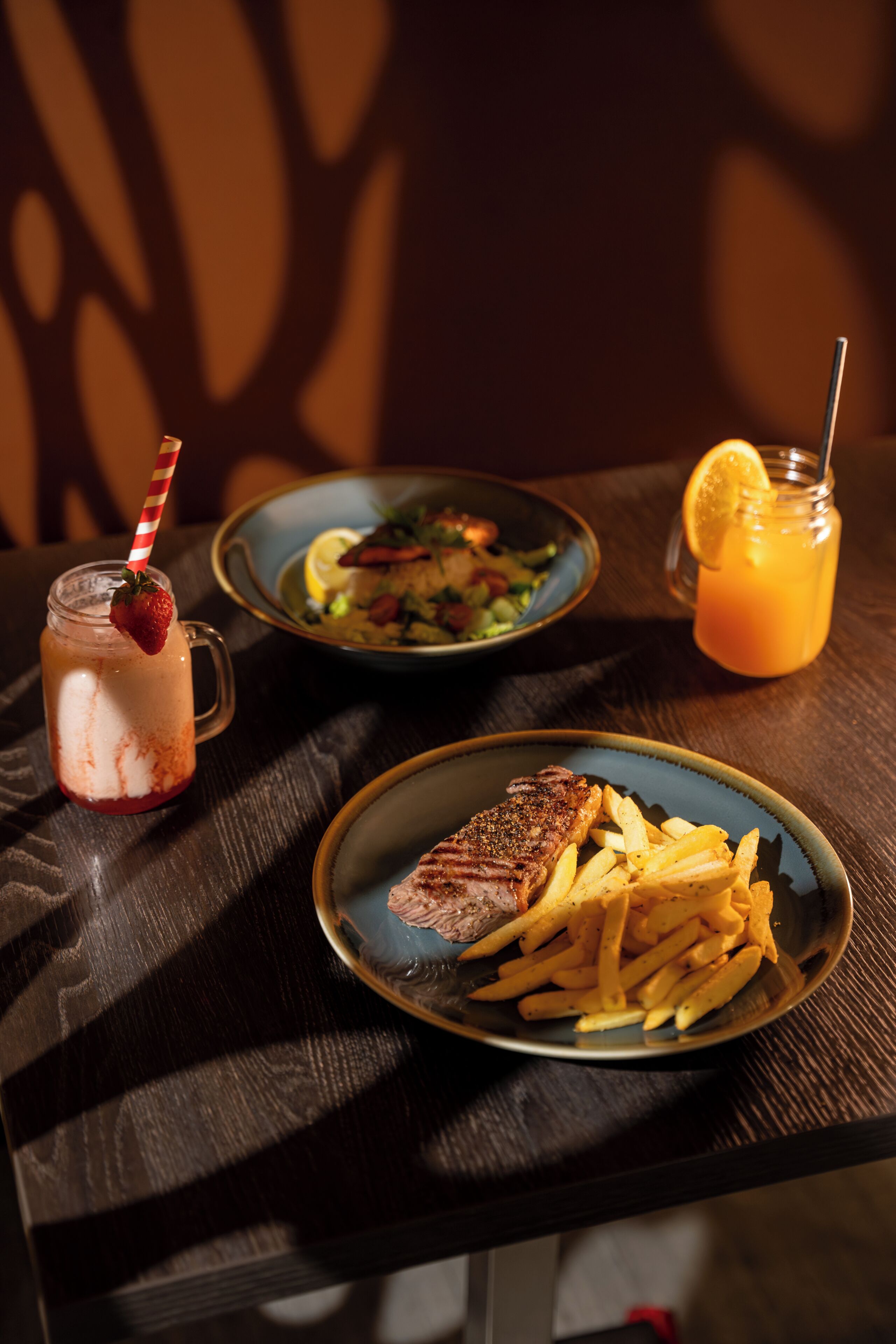 A table with a plate of steak and fries, a glass of iced drink with a straw, and a bowl of salad.