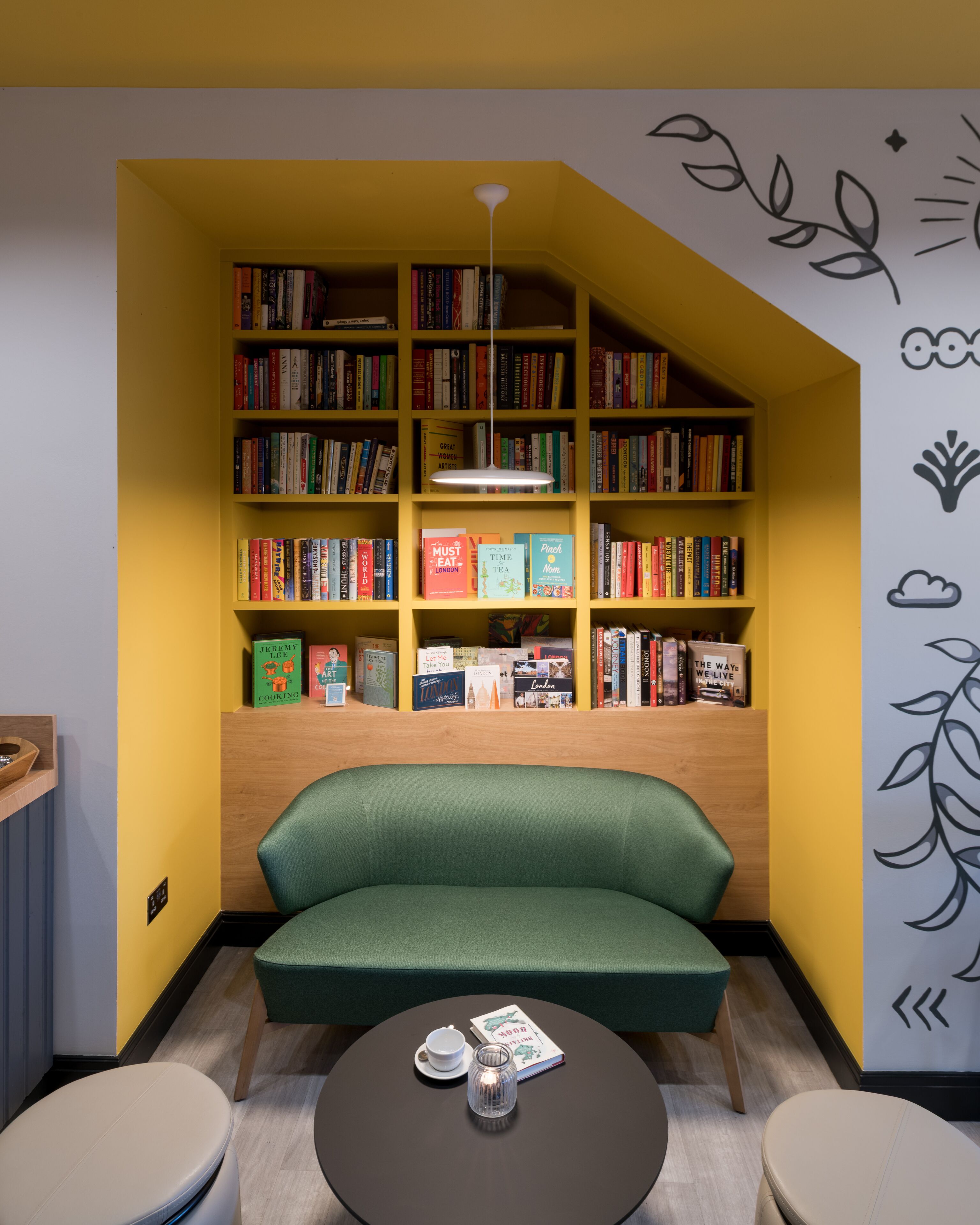 Un rincón acogedor para leer, con un sofá verde, una mesita con un libro y una taza, y una estantería llena de libros.