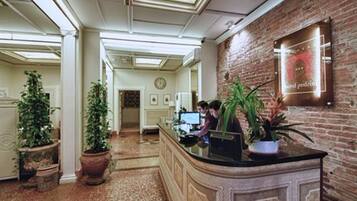 A hotel reception area with a brick wall, a reception desk, and potted plants.