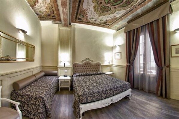 A hotel room with a large bed, a smaller sofa, a nightstand, and a mirror. - Hotel Pedrini (Bologna)