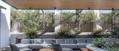A covered outdoor seating area with a stone floor, a wooden bench, and a built-in bench with a curved backrest.
