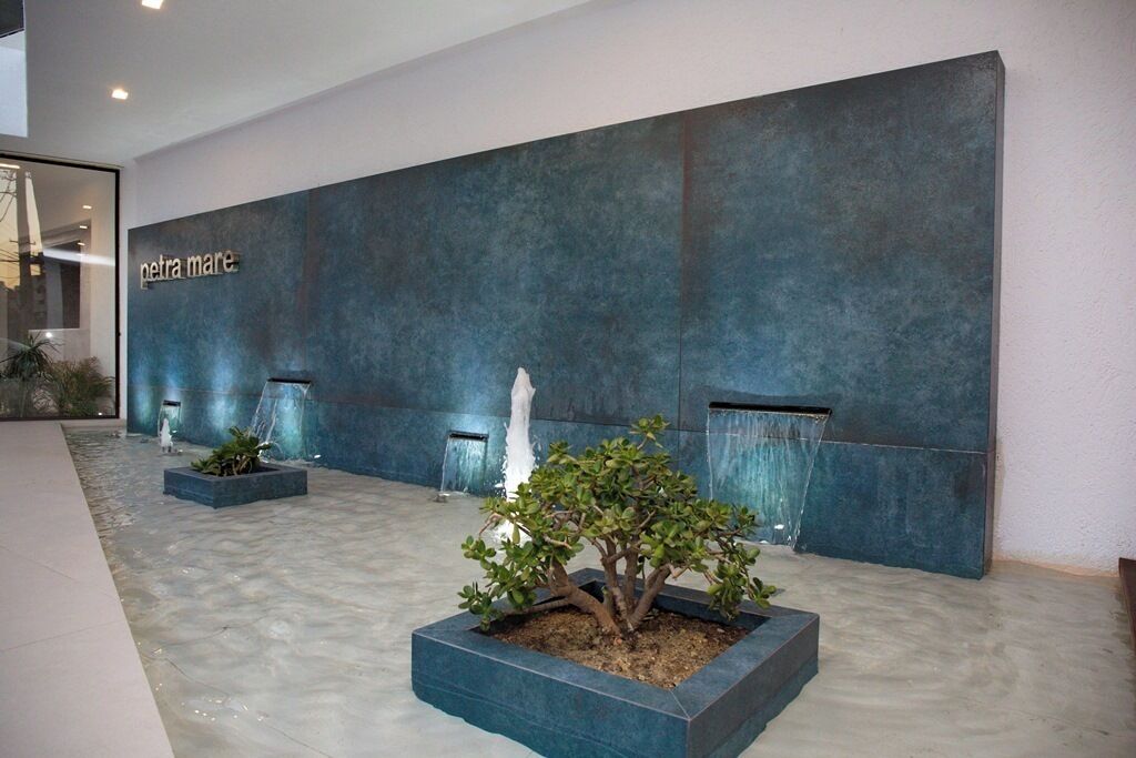 A reception area with a modern design, featuring a large wall with the name 'petra mare' and a small indoor garden with a bonsai tree.