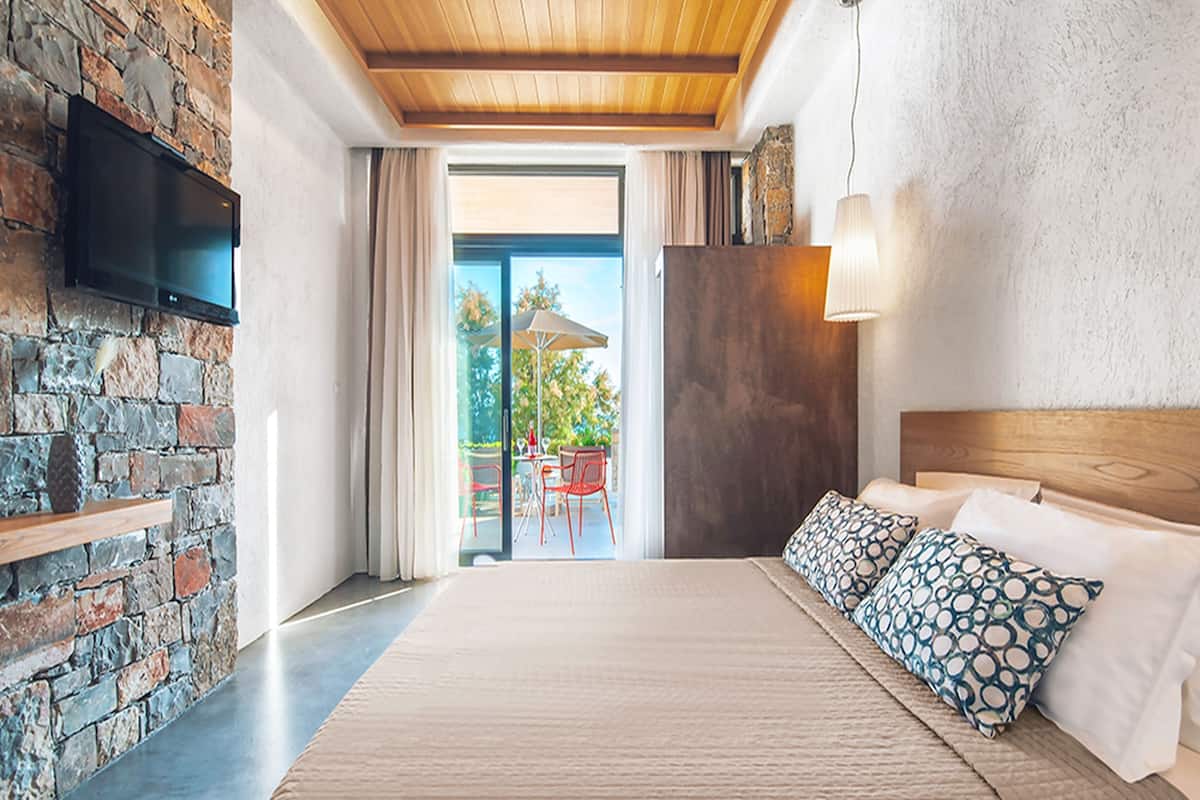 Un dormitorio con una cama grande, pared de piedra, televisor montado y vista al exterior.