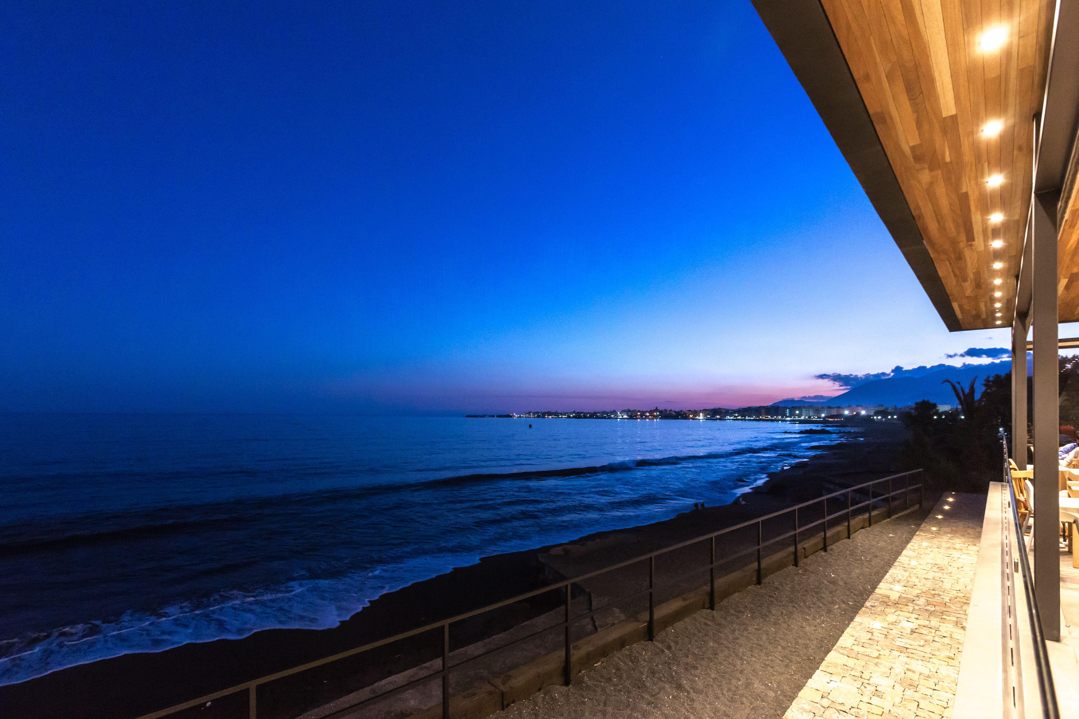 Une vue sur la côte depuis un balcon doté d’une balustrade, donnant sur la mer et sur une ville lointaine, au crépuscule.
