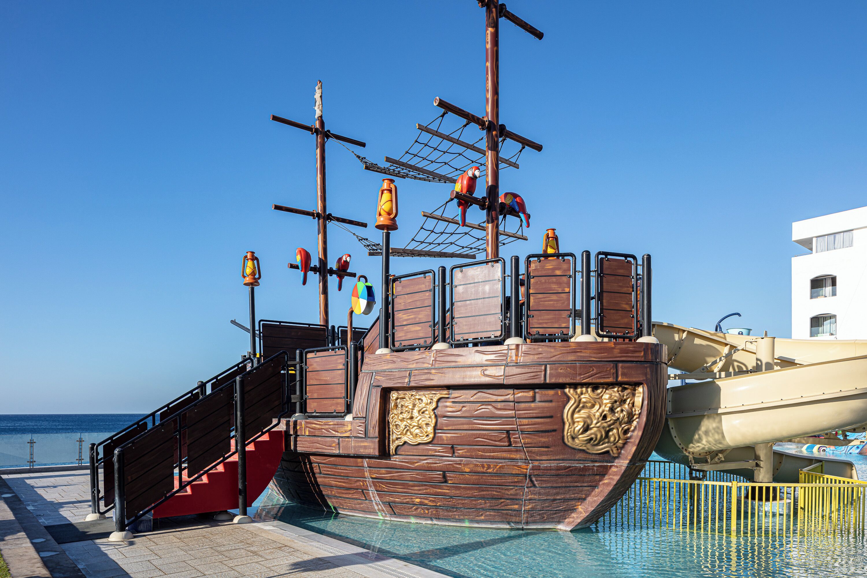 Eine hölzerne Piratenburg mit einer Treppe, die zu ihr hinaufführt, neben einem Schwimmbecken.