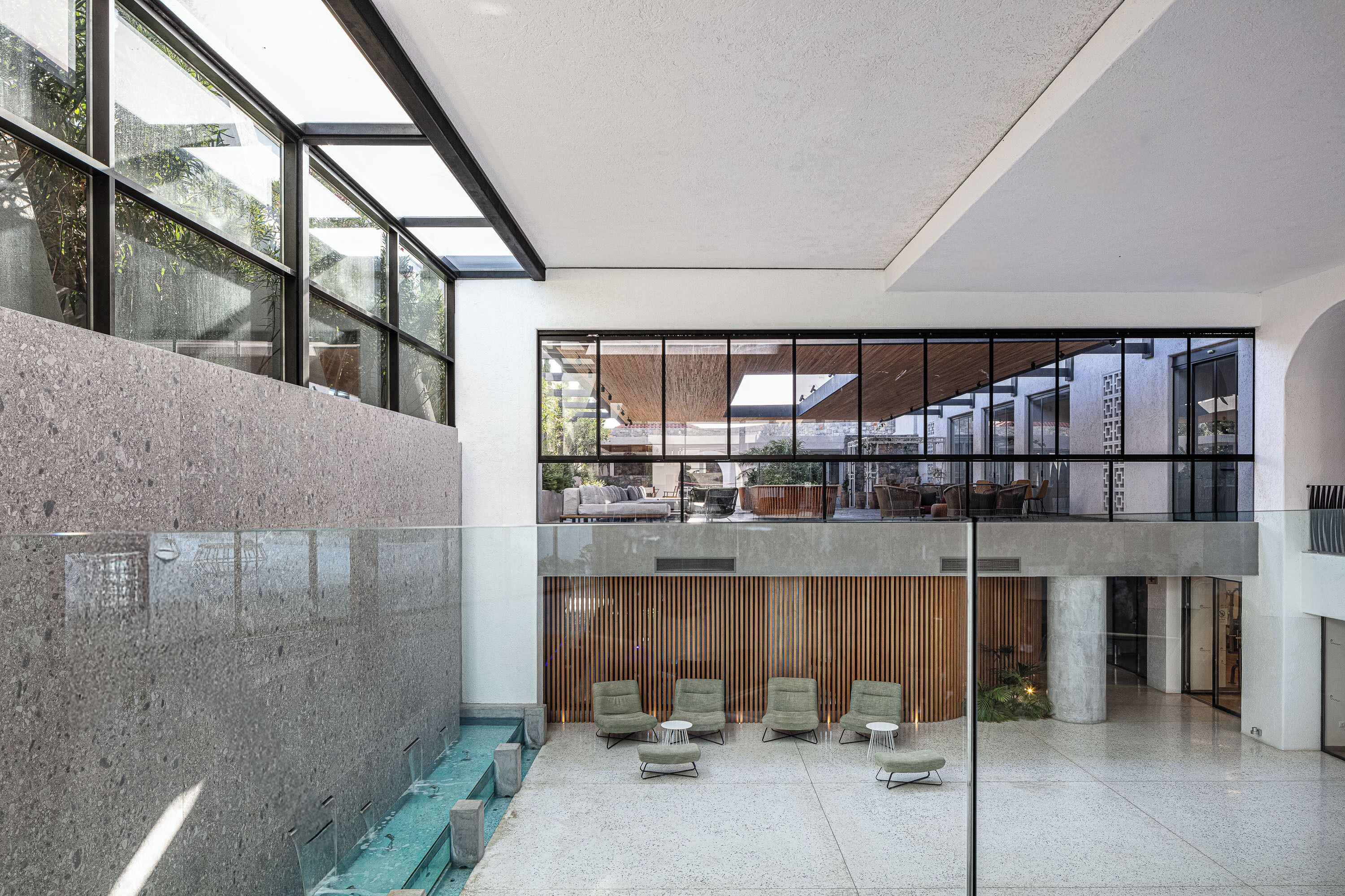 A modern interior with a glass atrium, seating area, and a pool.