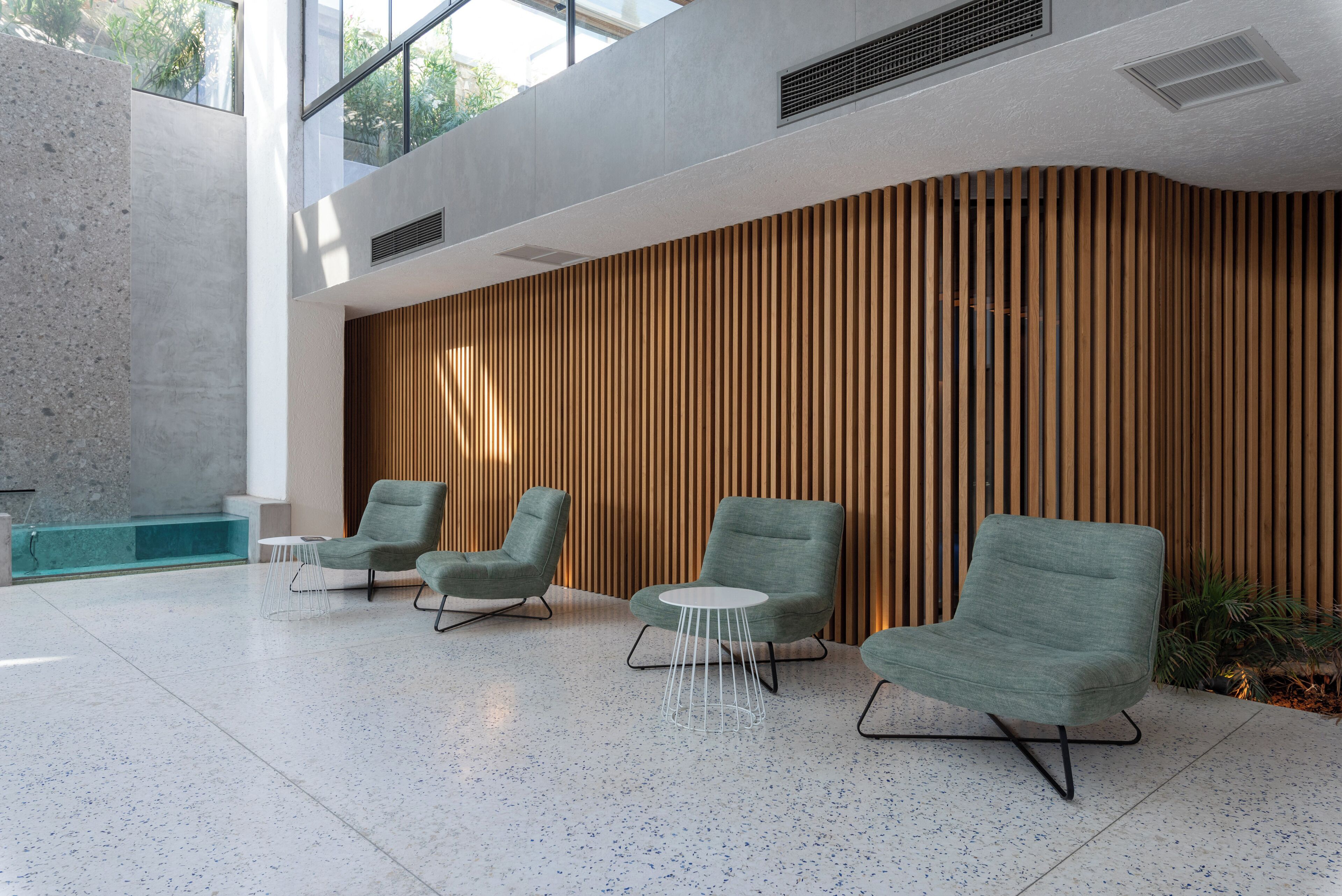 A modern lobby with three green armchairs, a small white table, and a wooden slatted wall.