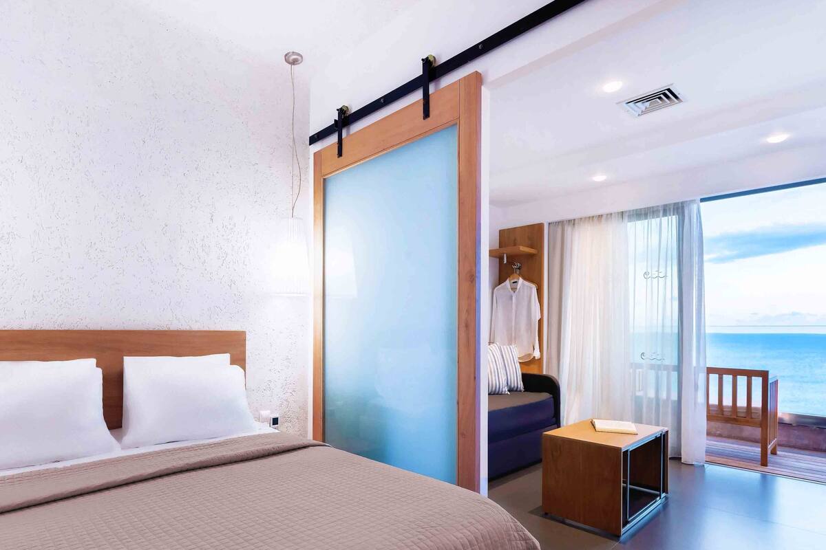 Una habitación de hotel moderna con una cama grande, un escritorio y un balcón con vista al mar.