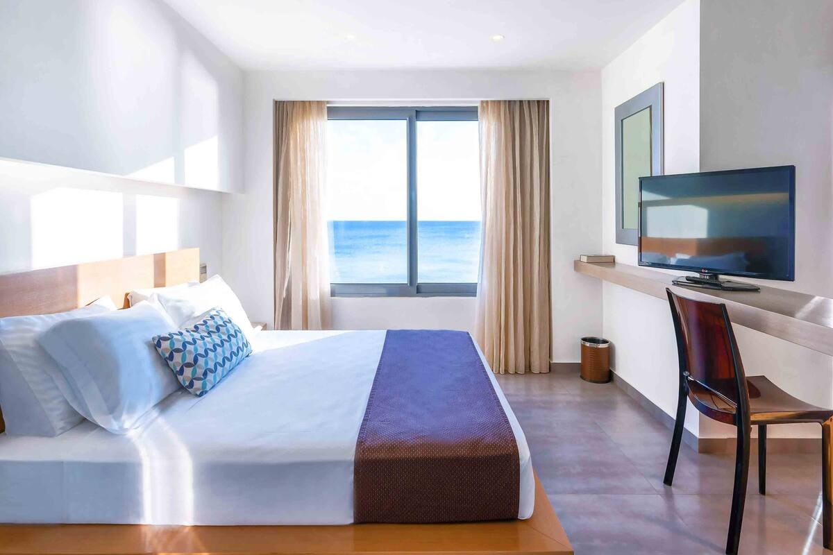 Habitación de hotel con una cama grande, televisión y vista al mar.