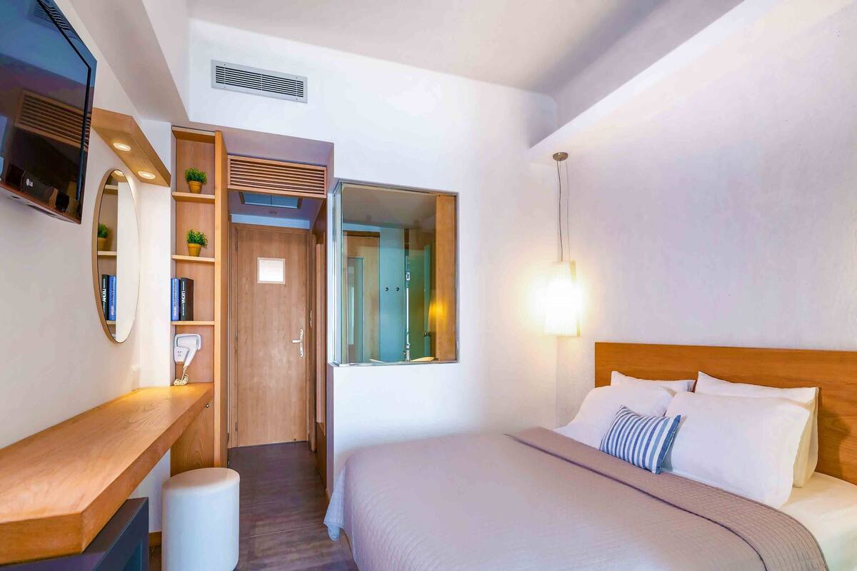 Una habitación de hotel con cama, mesita de noche, televisor y vestidor.