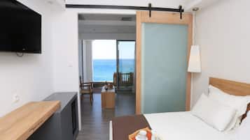 A hotel room with a bed, a desk, a TV, and a balcony with a view of the sea.