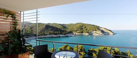 A balcony with wicker furniture and a view of a coastal landscape.