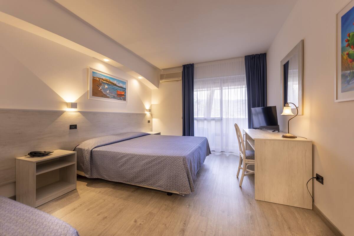 Ein modernes Hotelzimmer mit Bett, Schreibtisch und Stuhl, mit einem Gemälde an der Wand und einem fensterbepften Fenster.