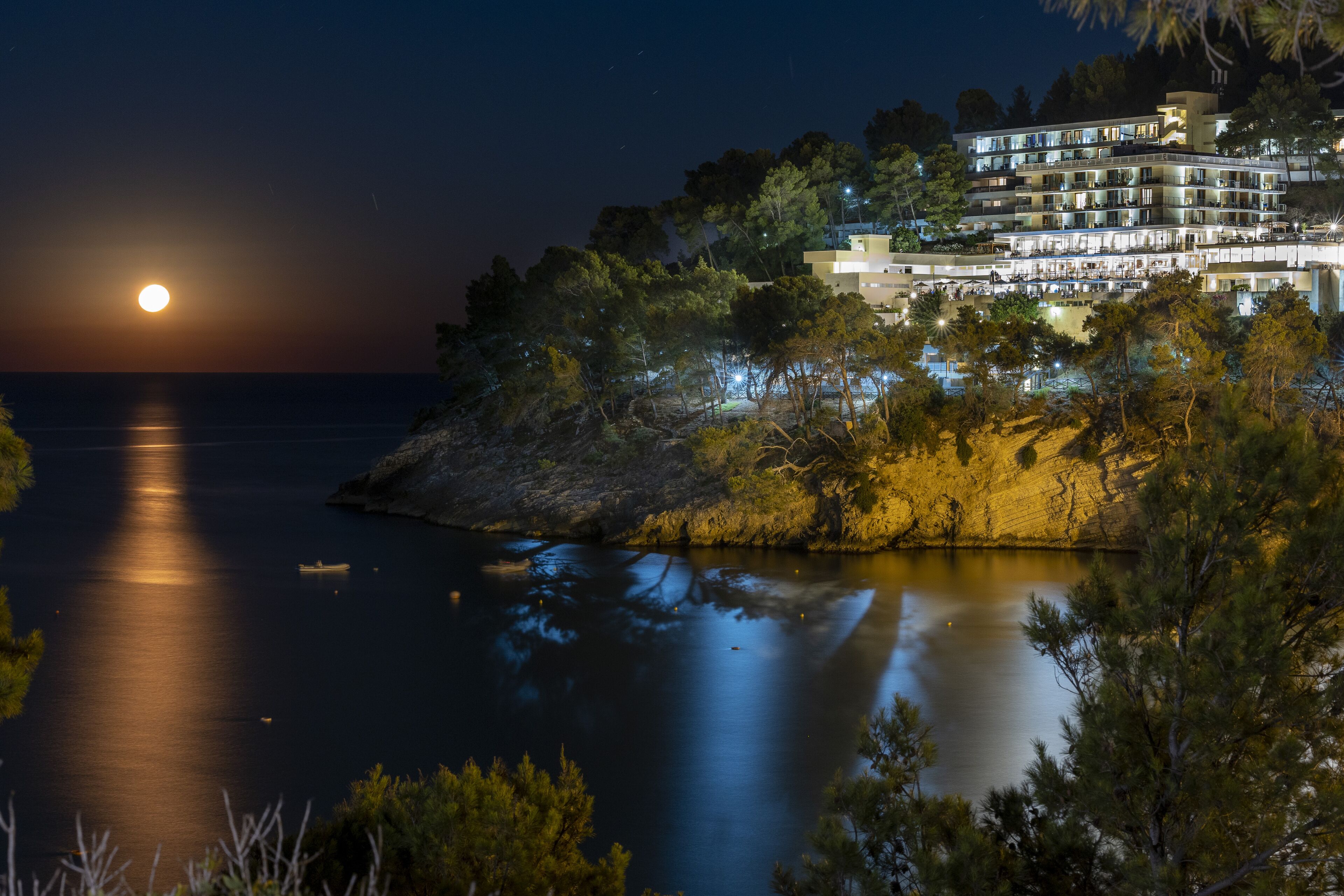 Ein Hotel an der Küste mit mehreren Balkonen mit Meerblick, eine mondbeschienene Nacht und der Gebäuderielection im ruhigen Wasser.