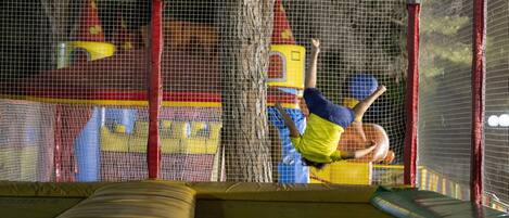 A trampoline with safety netting and padded walls, indicating a play area.
