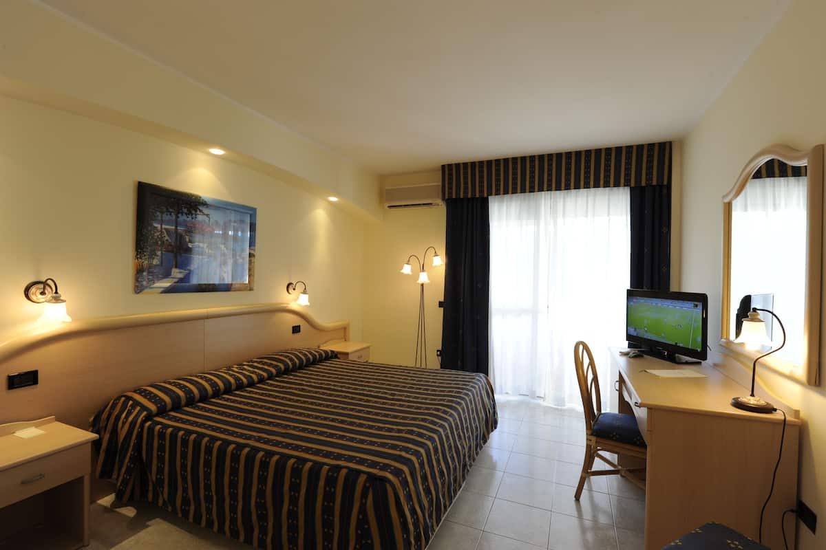 Ein Hotelzimmer mit Bett, Schreibtisch, Stuhl, Fernseher und Kunstwerk an der Wand.