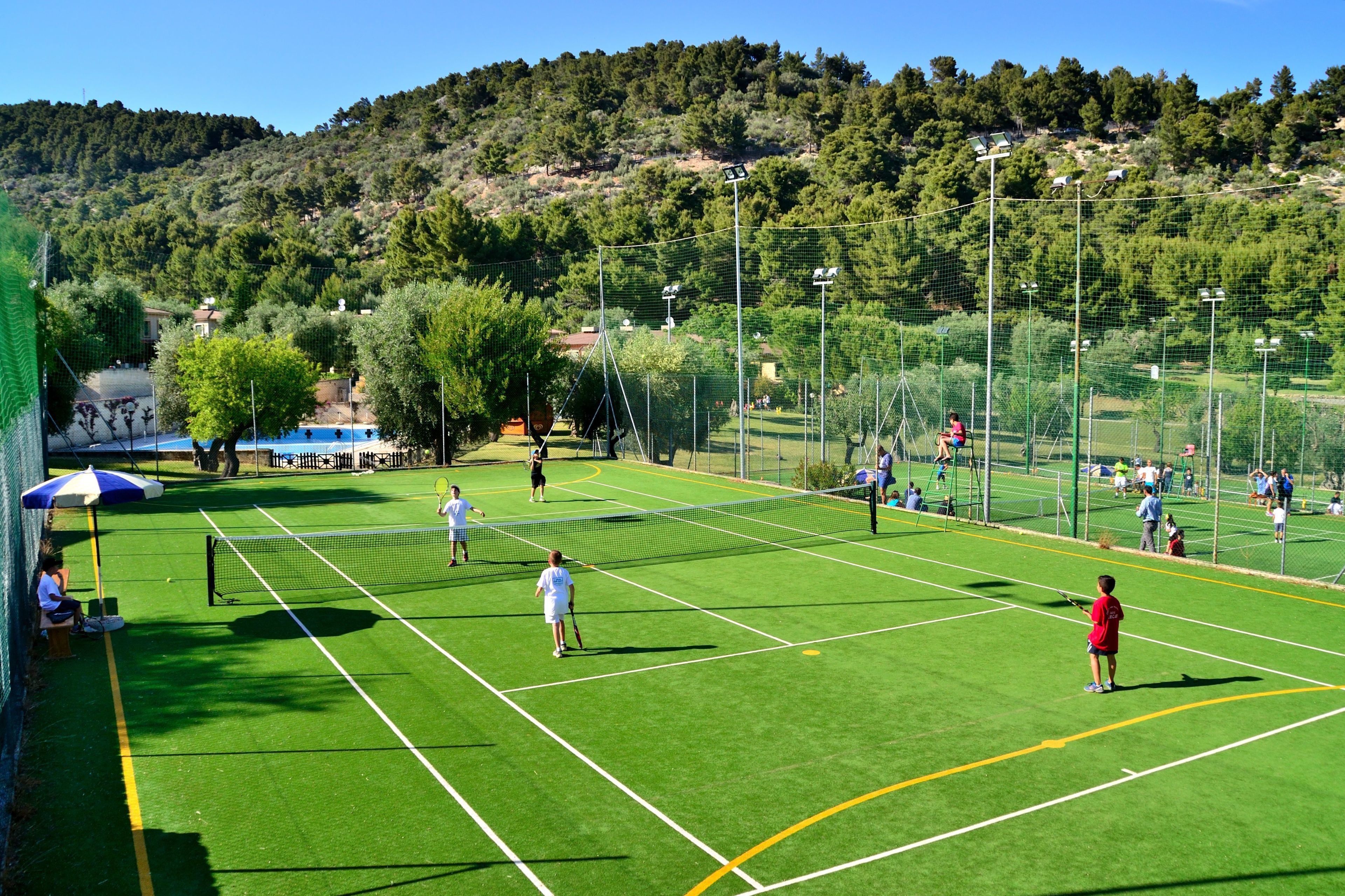 A tennis court with players, a net, and a green field.