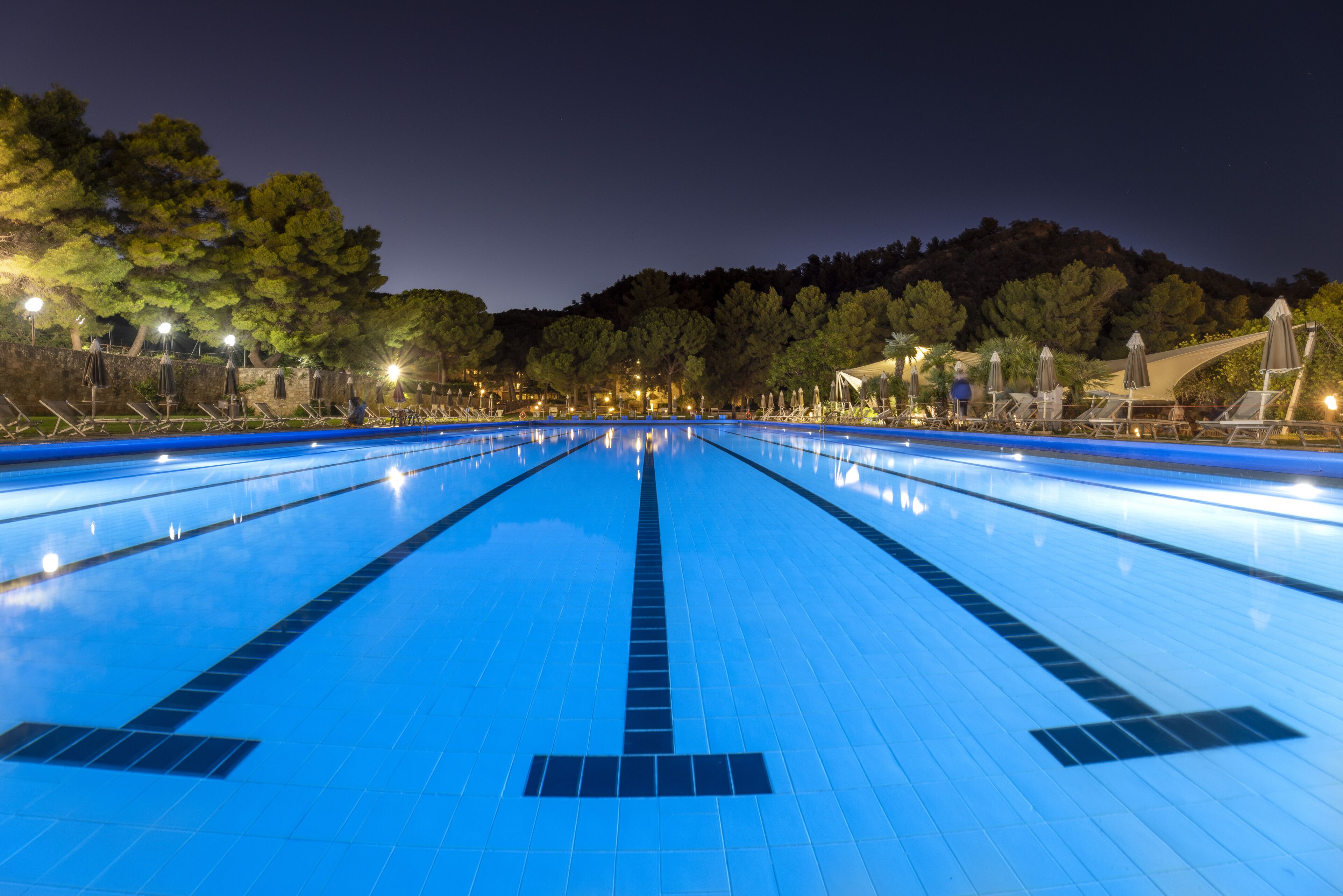 A swimming pool with clear lanes, surrounded by trees and outdoor seating areas.