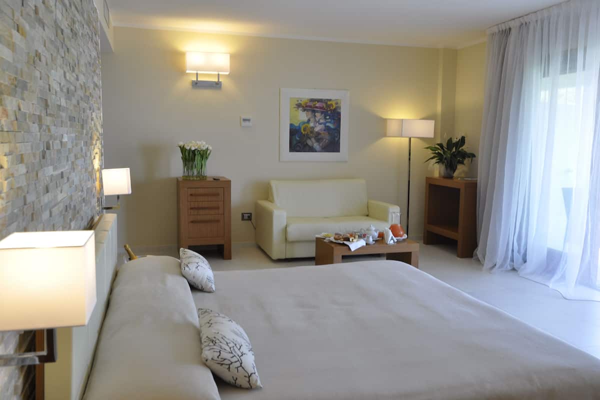 Ein Hotelzimmer mit einem großen Bett, einer Couch, einem kleinen Tisch und einer Lampe. An der Wand hängt ein Gemälde und das Fenster ist mit Vorhängen versehen.