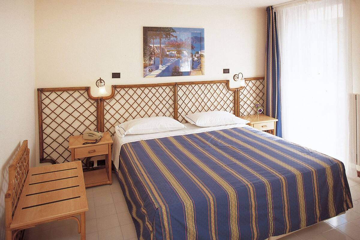 Ein Hotelzimmer mit einem Bett, zwei Nachttischen, einem Sessel und einem Bild an der Wand.
