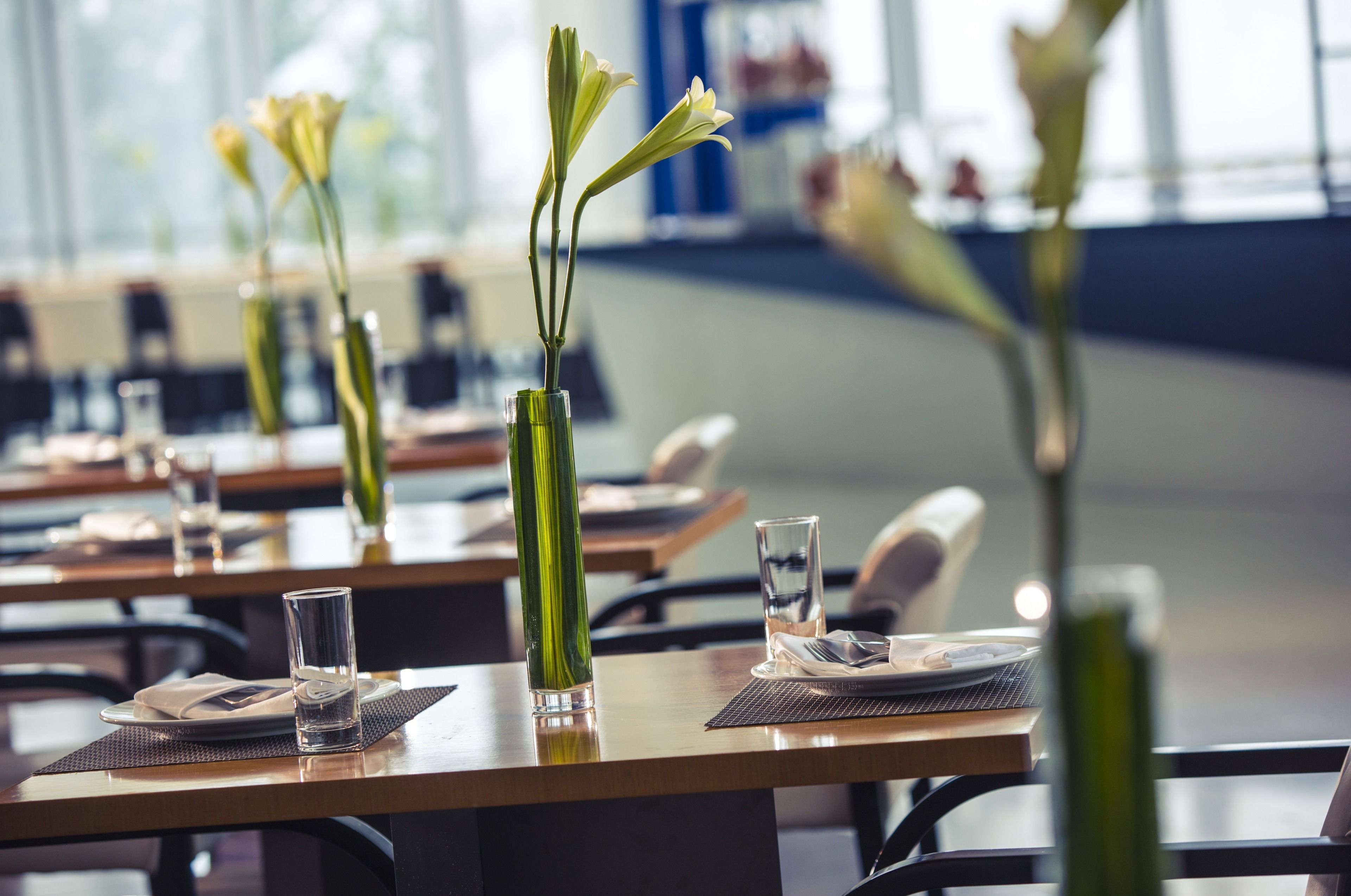 Um restaurante com mesas postas, pratos, copos e vasos de flores.