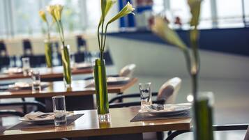 Um restaurante com mesas postas, pratos, copos e vasos de flores.