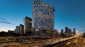 A modern high-rise building with a glass facade and illuminated windows, surrounded by a busy urban street with moving traffic. - Renaissance Beijing Capital Hotel (Beijing)