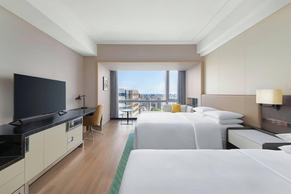 A hotel room with a large bed, a TV, a desk, and a view of the city.