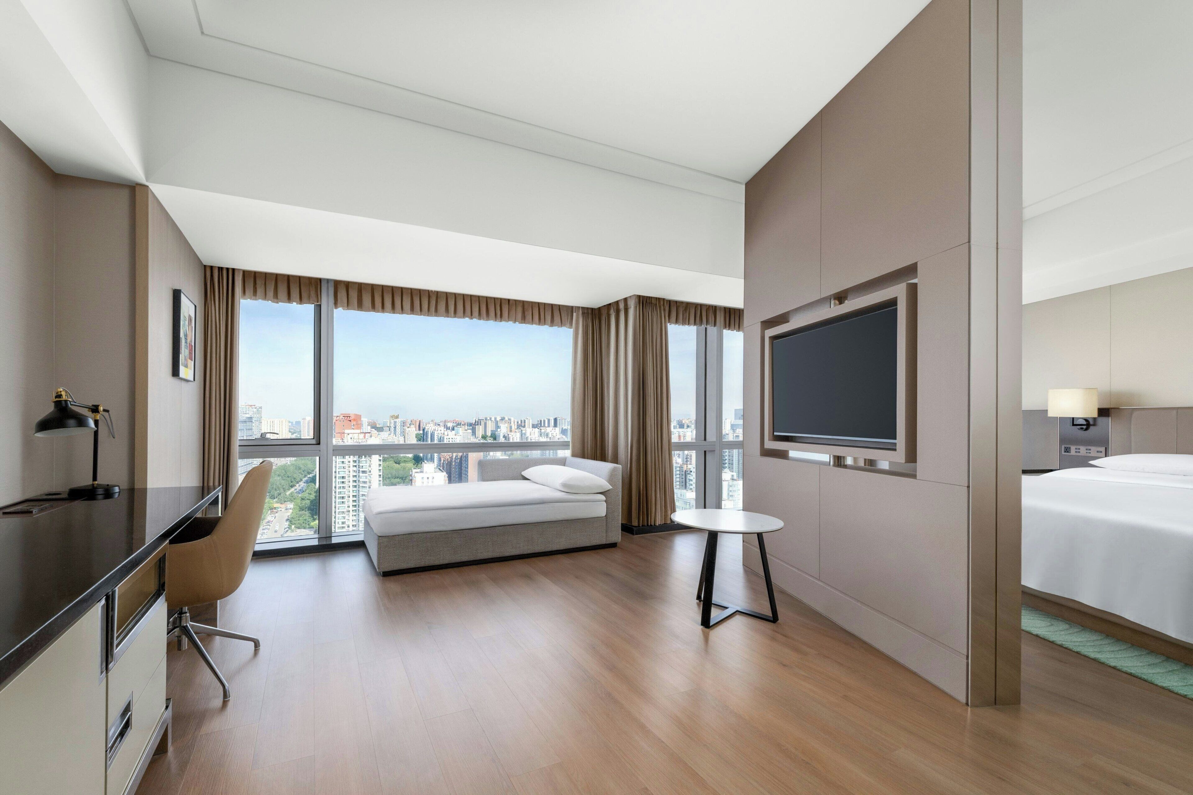 A hotel room with a bed, a desk, a chair, a TV, and a window with a city view.