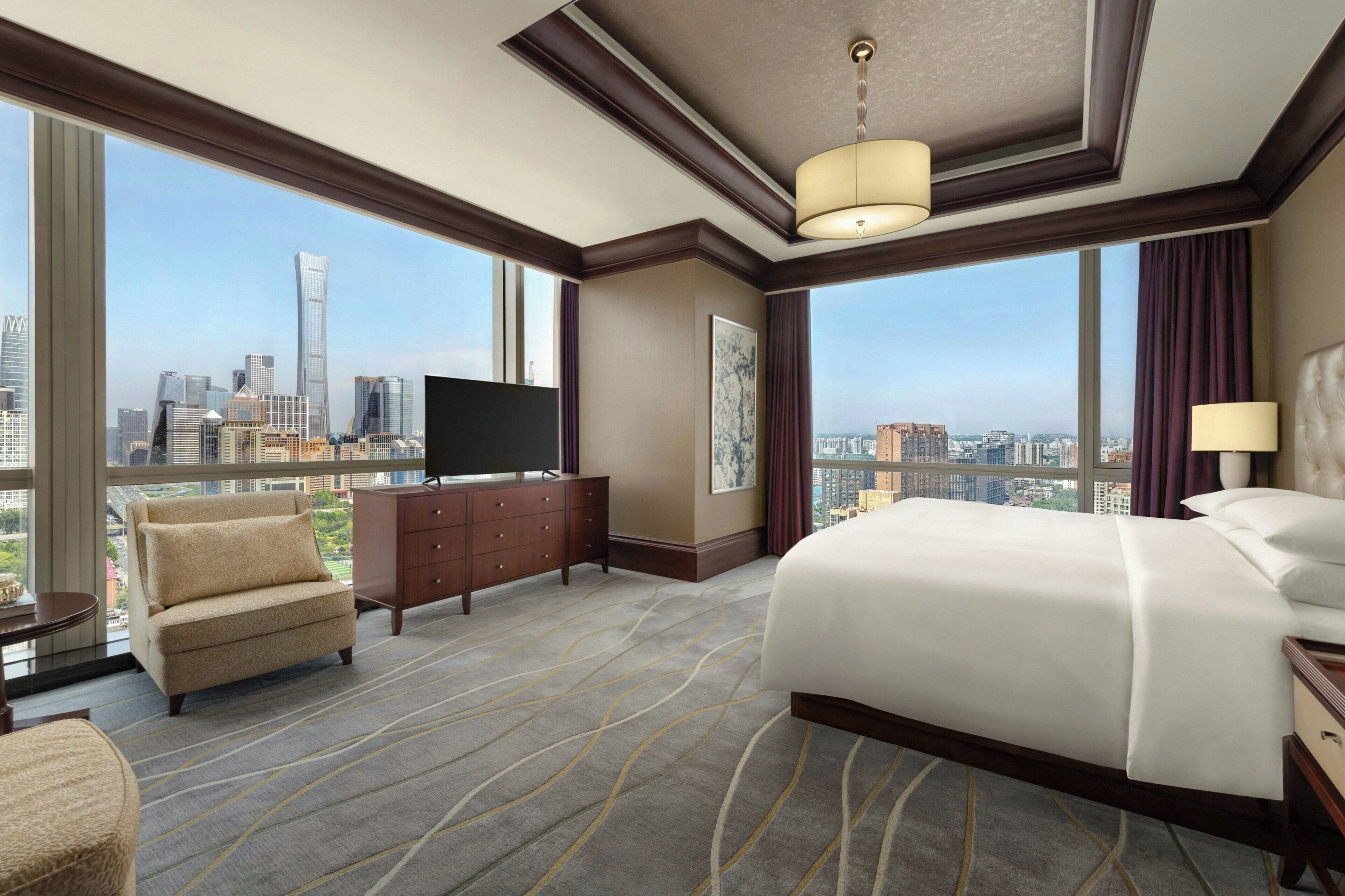 Une chambre d’hôtel avec un grand lit, un téléviseur posé sur une commode, un canapé et une vue sur les toits de la ville.
