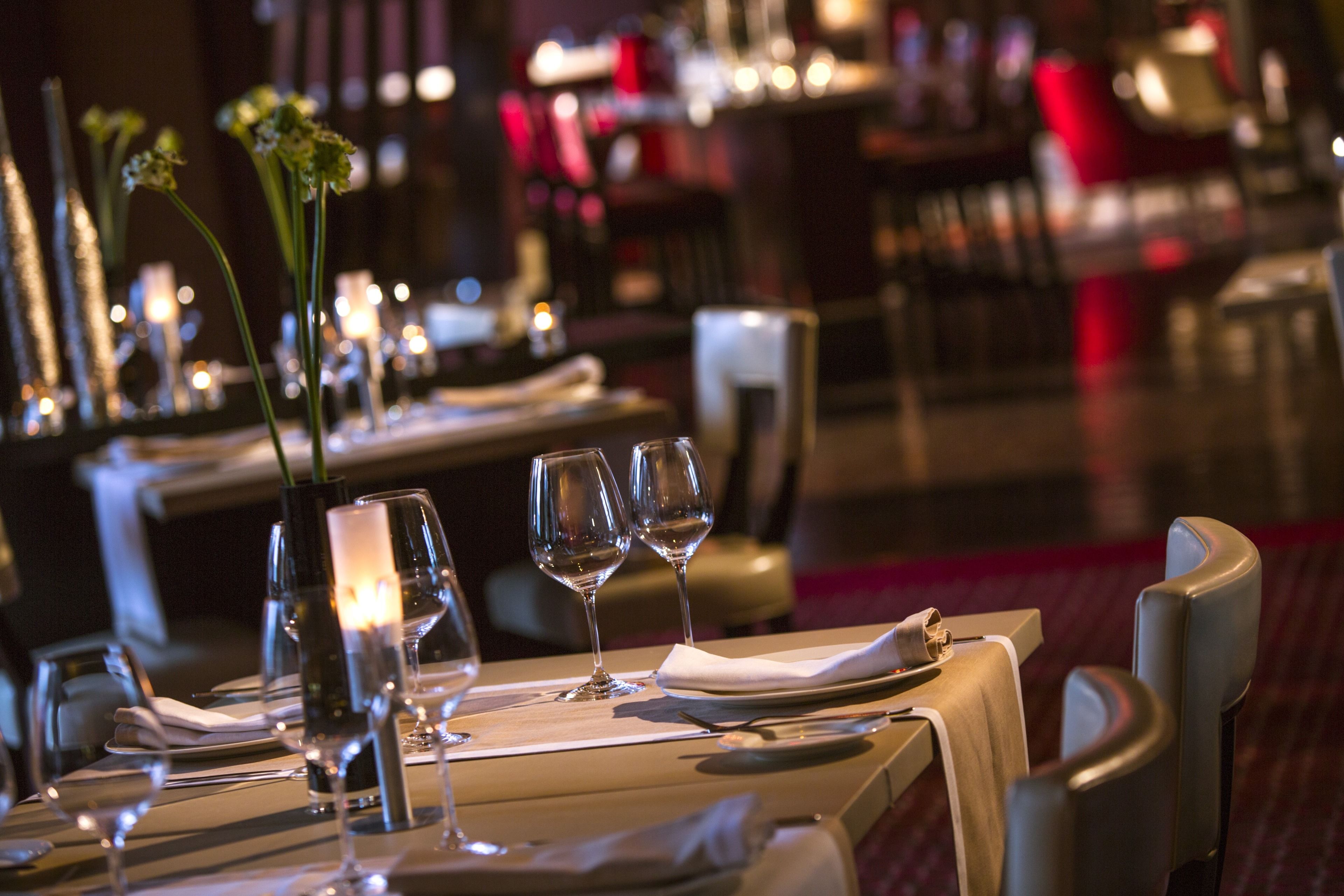 A restaurant setting with tables set for dining, featuring candles and glassware.