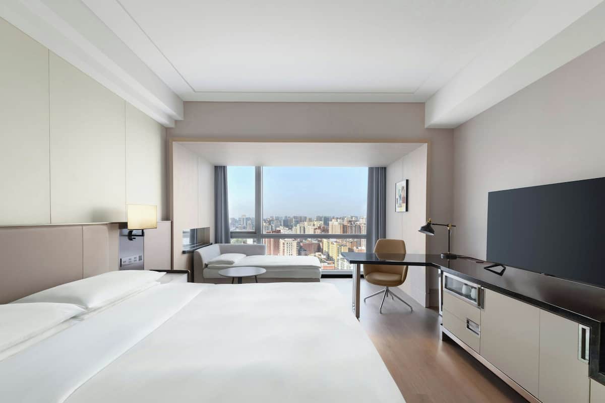 A hotel room with a bed, a sofa, a desk, a chair, a TV, and a city view.