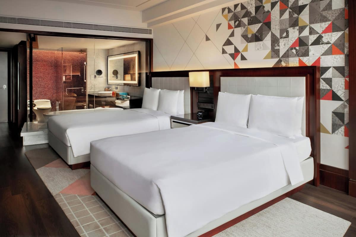 A hotel room with two beds, a large mirror, a nightstand, and a geometric-patterned wall.