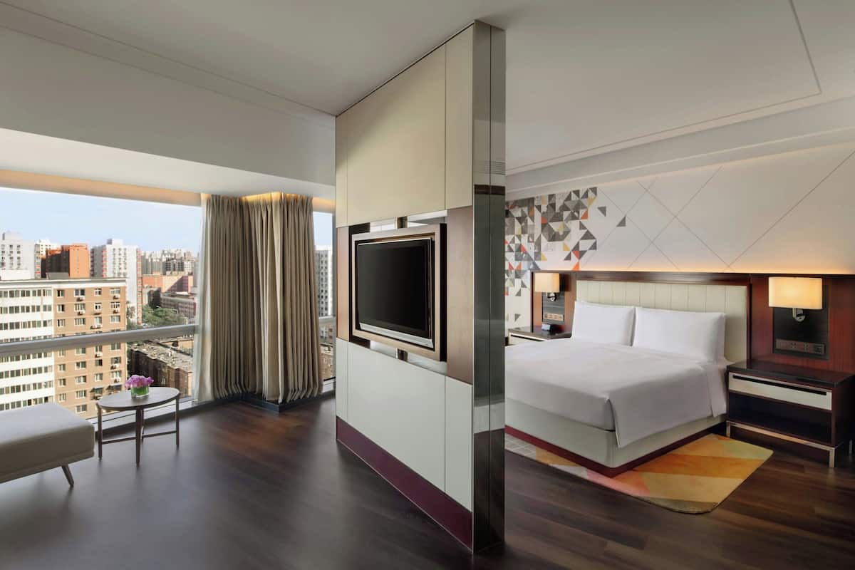 A hotel room with a large bed, a TV, a desk, and a view of the city.