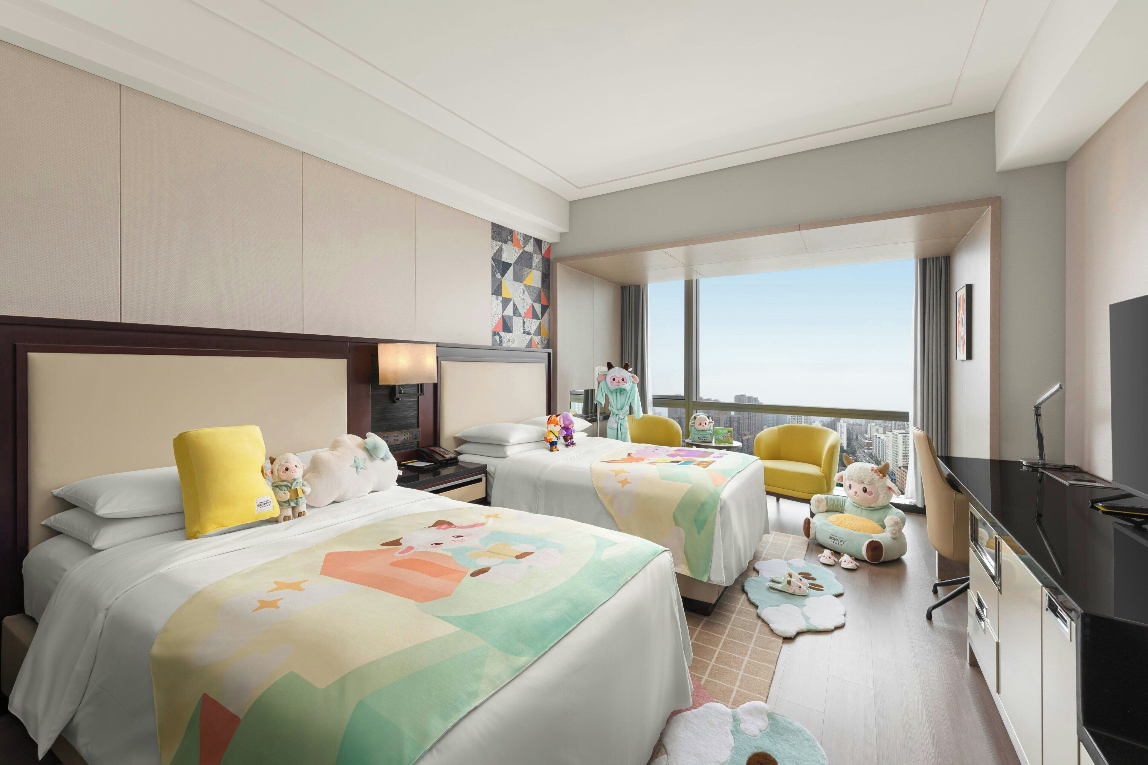 Habitación de hotel con dos camas, un escritorio, una silla, un televisor y un ventanal grande.