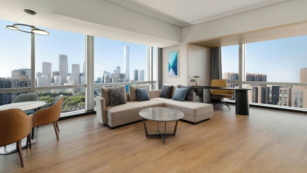A spacious living room with a large sectional sofa, a glass coffee table, and a view of a city skyline through large windows. - Renaissance Beijing Capital Hotel (Beijing)