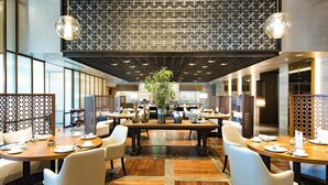 A modern dining area with wooden tables, white chairs, and a central plant. - Renaissance Beijing Capital Hotel (Beijing)