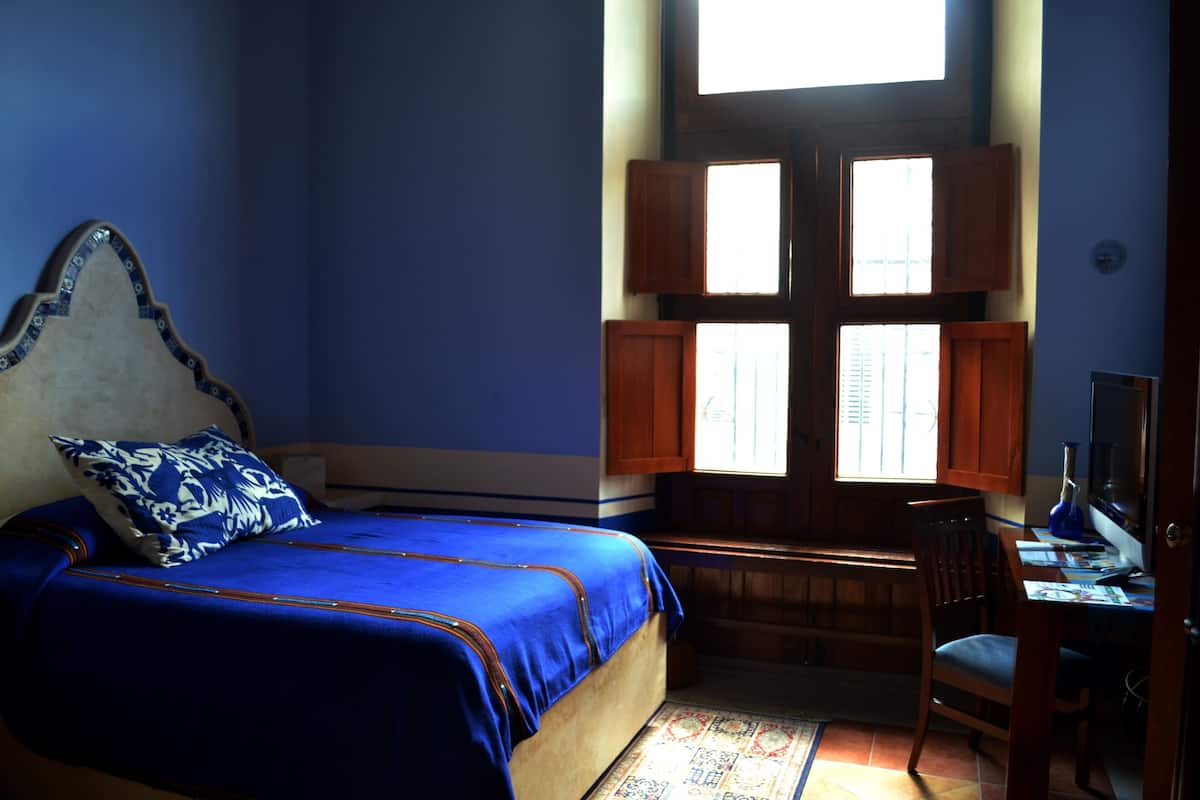 Un dormitorio con cama, escritorio y ventana con contraventanas.