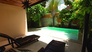 Zona junto a la piscina con sillas de descanso y vistas a una piscina rodeada de exuberante vegetación.