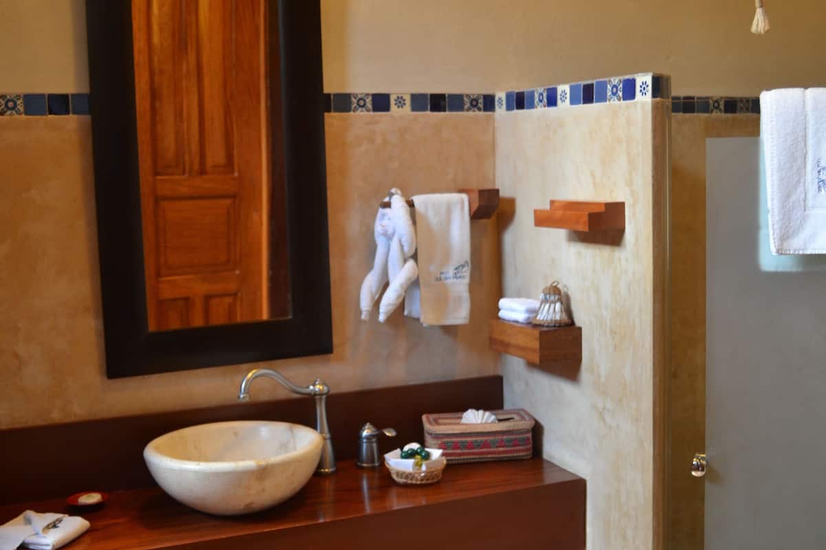 Un baño con un espejo grande, un lavabo sobre encimera, un mueble de tocador de madera, un perchero y una zona de ducha.