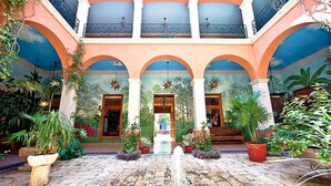 Un patio con una fuente, plantas en macetas y un mural en las paredes.