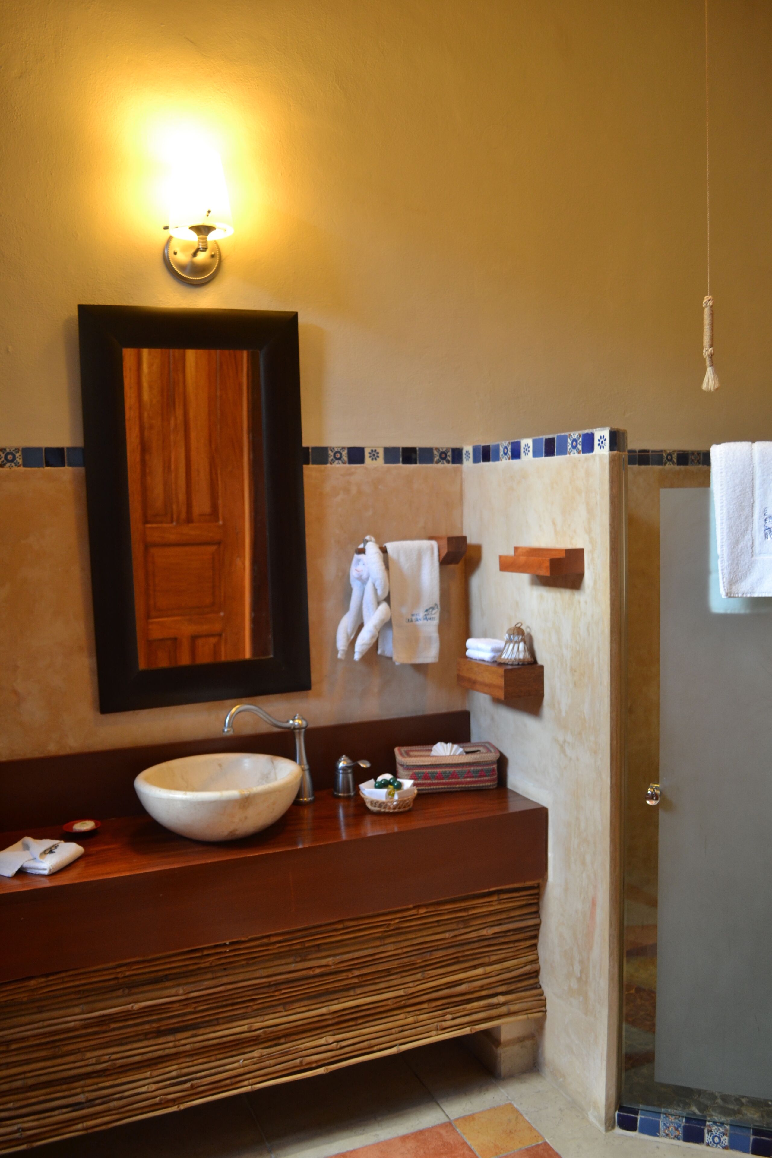Un baño con un espejo grande, un lavabo sobre encimera, un mueble de tocador de madera, un perchero y una zona de ducha.