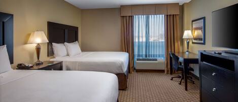 A hotel room with two beds, a desk, a chair, a TV, and an air conditioning unit.