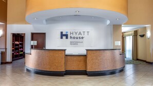 A Hyatt House reception desk with a curved design, a white wall with the hotel name, and a wooden reception area. - Hyatt House Bentonville/Rogers (Rogers)